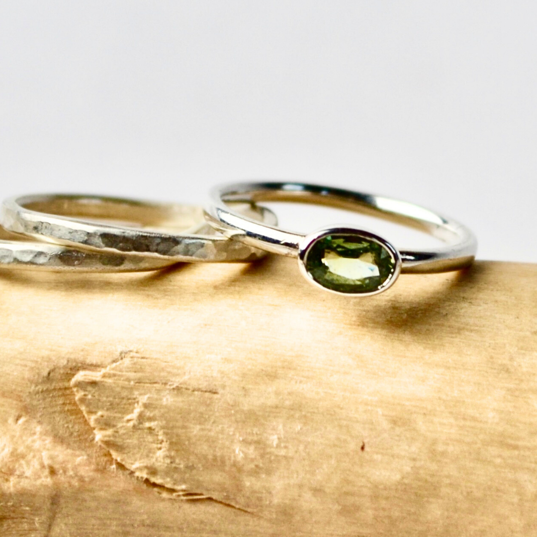 Two rings, one gold and one silver with a green stone, on a wooden surface.
