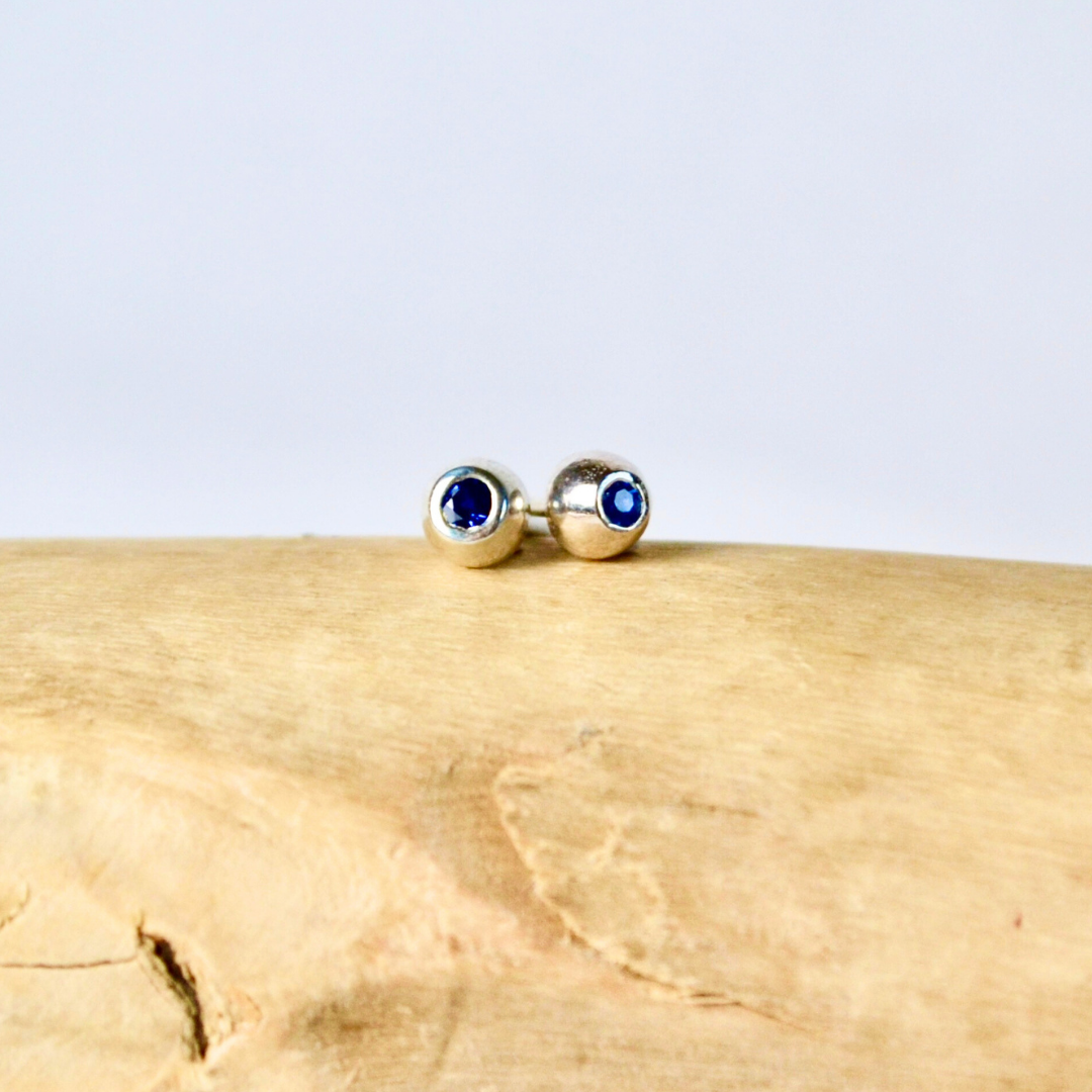 Gold stud earrings with blue gemstones on a wooden surface