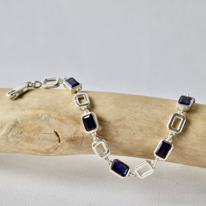 Silver bracelet with blue stones on a piece of driftwood against a light gray background