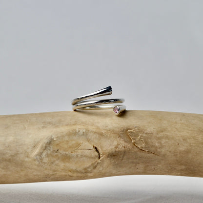 Silver ring with a small gemstone on a piece of driftwood against a gray background