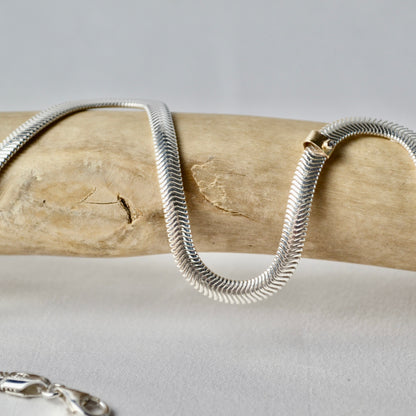 Silver snake chain necklace on a wooden stick with a neutral background