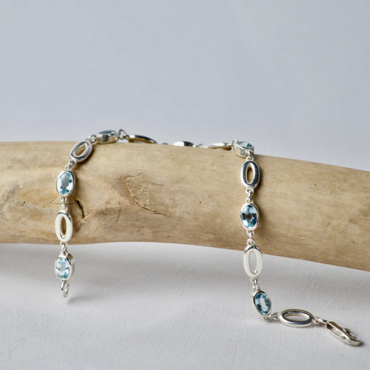 Silver bracelet with blue gemstones on a wooden branch against a light background