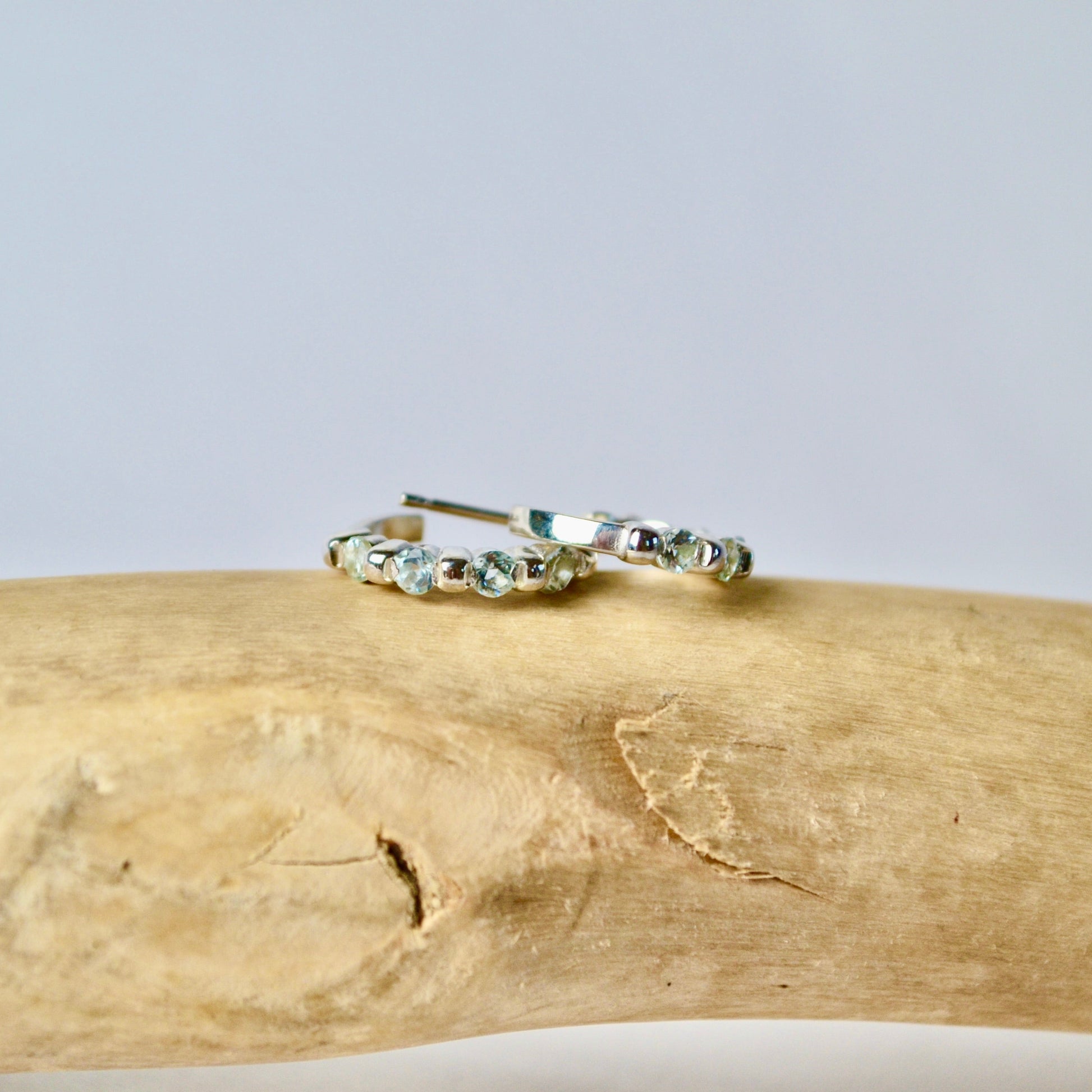 Gold hoop earrings with green gemstones on a wooden surface