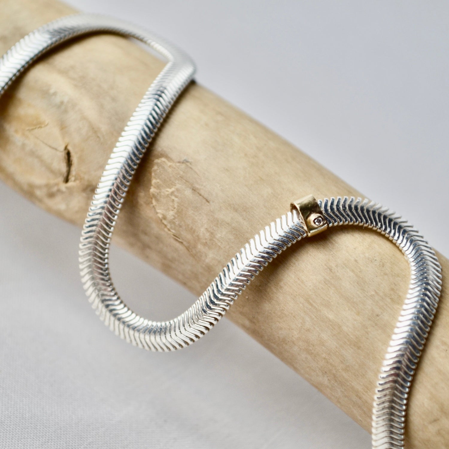 Silver snake chain necklace on a wooden branch with a neutral background