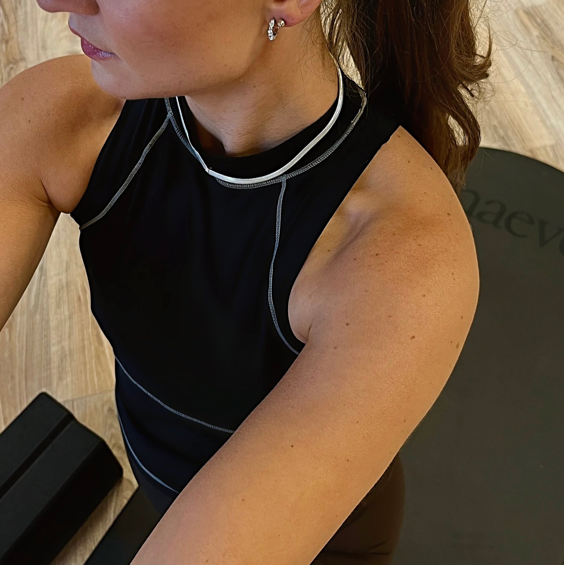 Person wearing a black sleeveless top with white trim, sitting on a yoga mat.