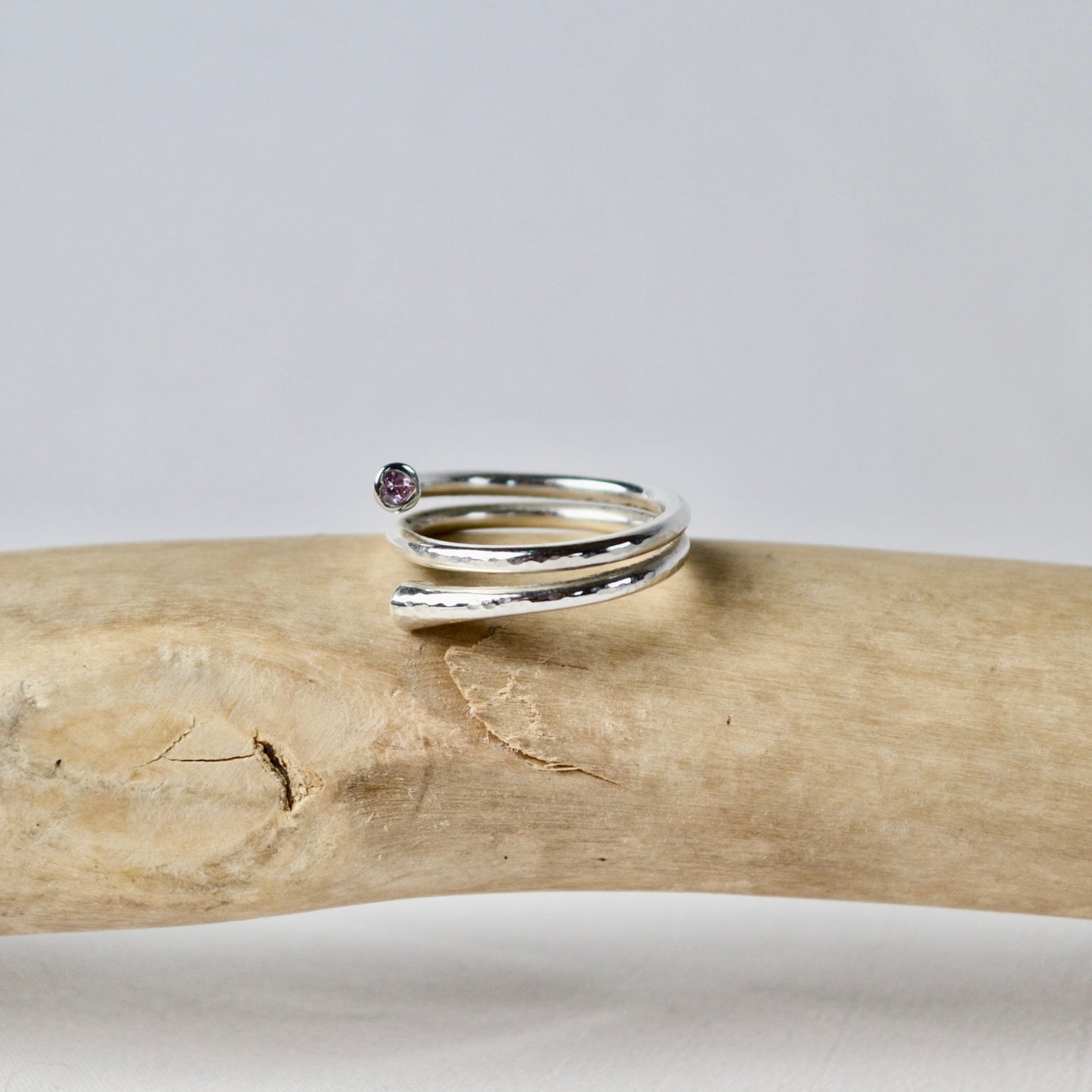 Silver ring with a small gemstone on a piece of driftwood against a gray background