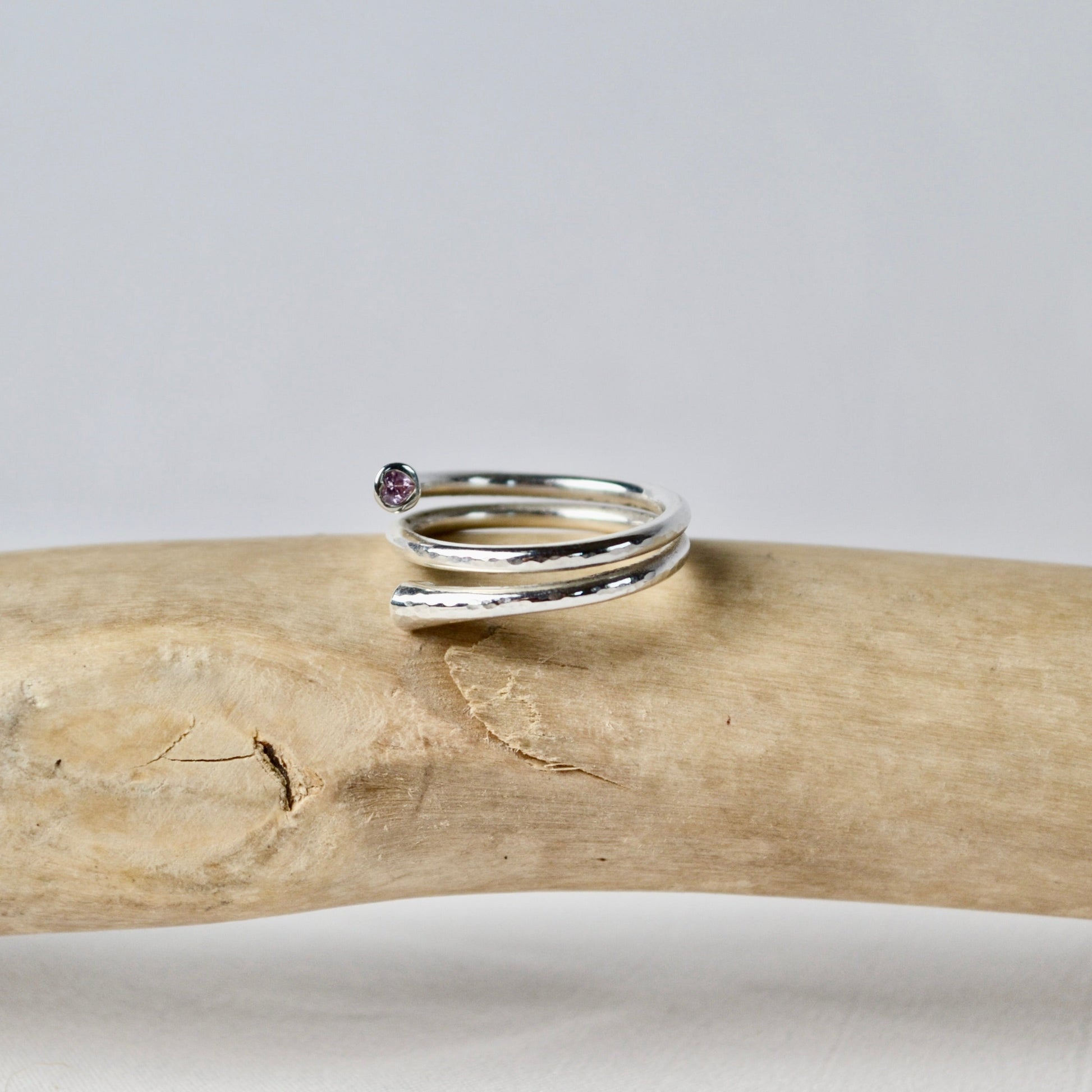 Silver ring with a small gemstone on a piece of driftwood against a gray background