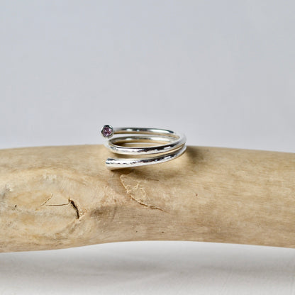 Silver ring with a small gemstone on a piece of driftwood against a gray background