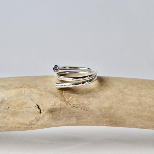 Silver ring with a small gemstone on a piece of driftwood against a gray background