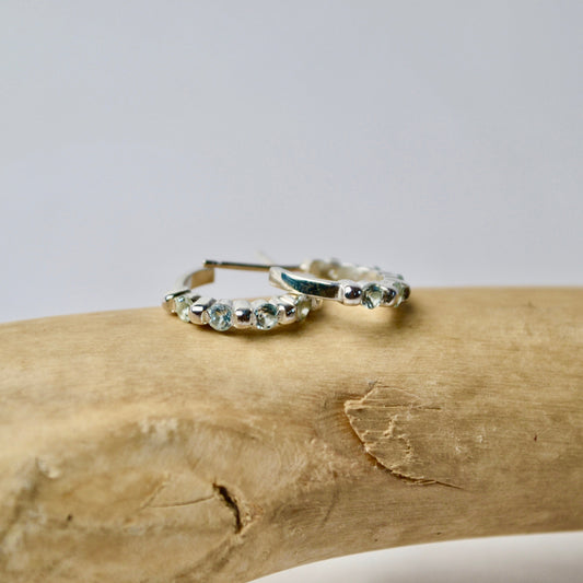 Silver hoop earrings with gemstones on a wooden surface