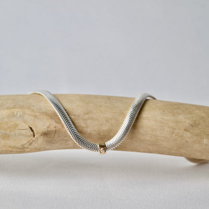 Silver snake chain necklace on a wooden branch with a plain background