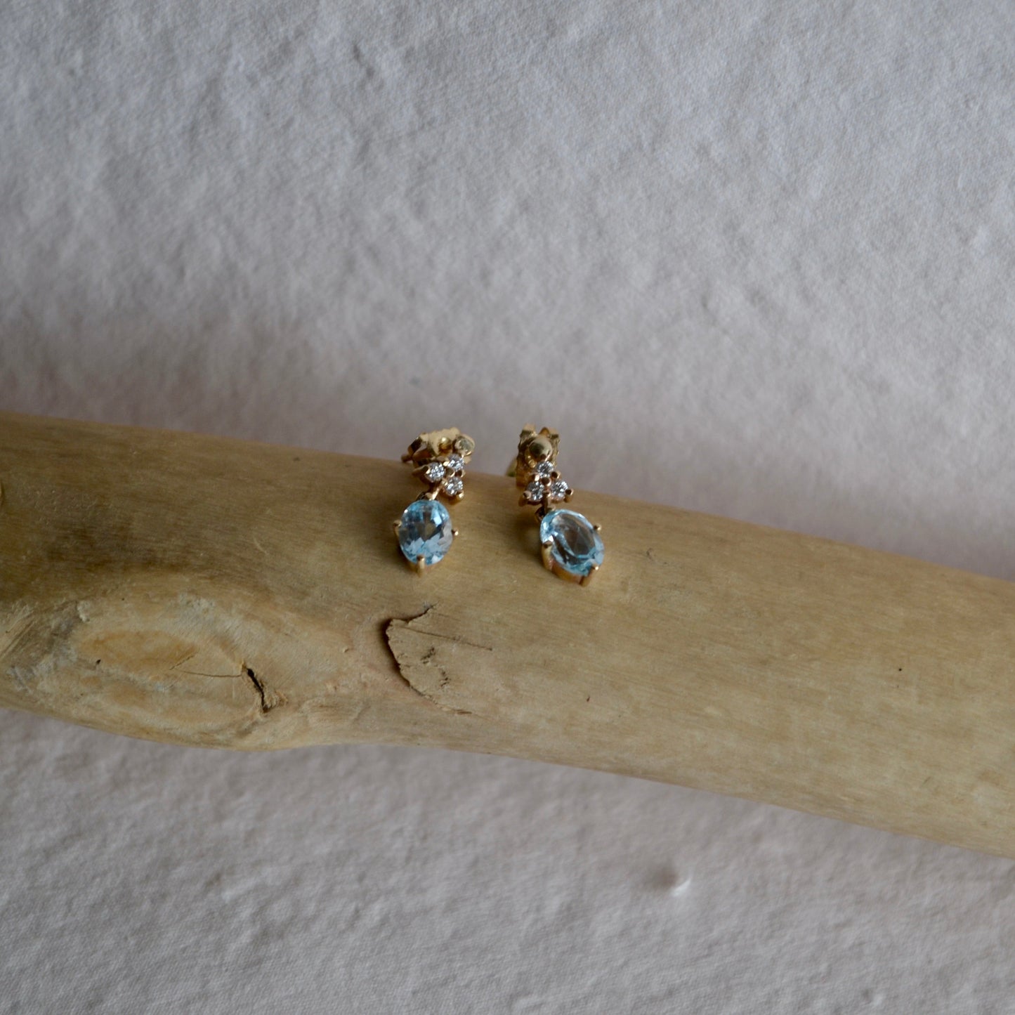 Pair of earrings with gemstones on a wooden stick against a plain background
