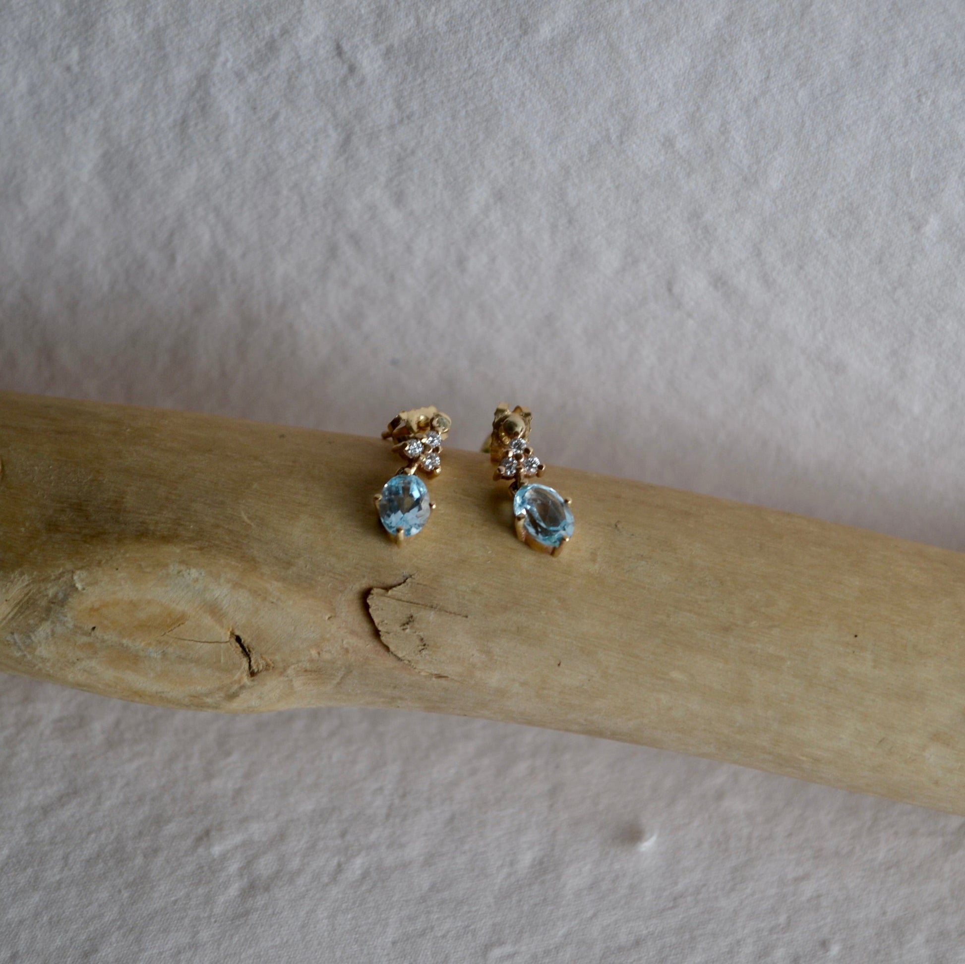 Pair of earrings with gemstones on a wooden stick against a plain background