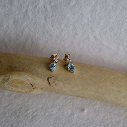 Pair of earrings with gemstones on a wooden stick against a plain background