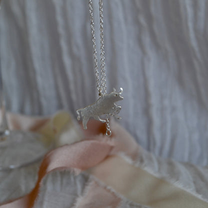 Silver unicorn necklace held by a hand with a blurred background