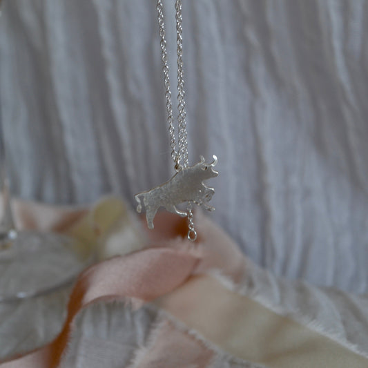 Silver unicorn necklace held by a hand with a blurred background