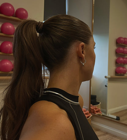 Woman with a ponytail in a gym setting with exercise balls on shelves.