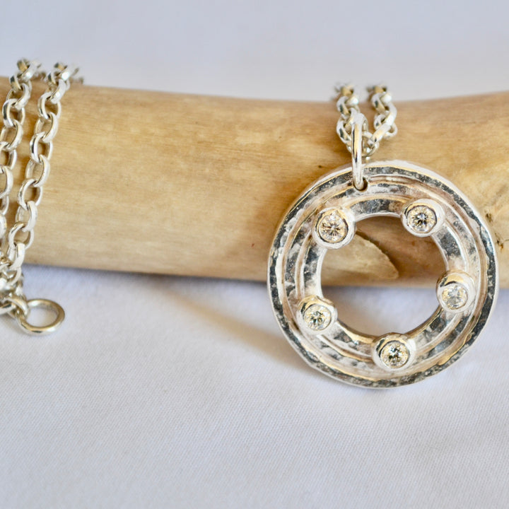 Silver necklace with a circular pendant on a wooden stick