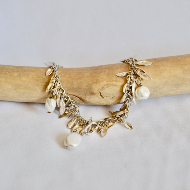 Gold bracelet with leaf and pearl charms on a wooden stick against a light background