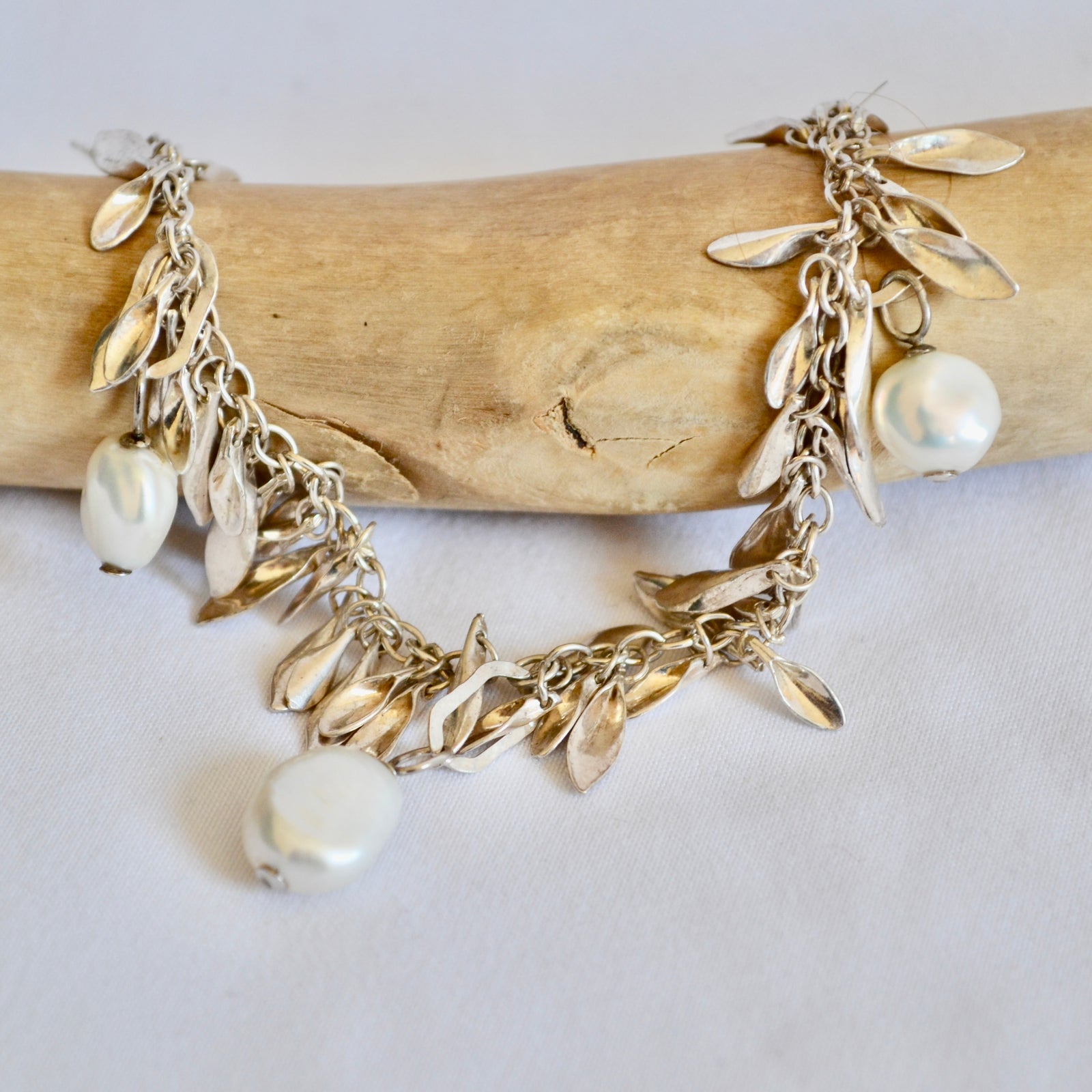 Bracelet with leaf and pearl charms on a wooden stick against a white background