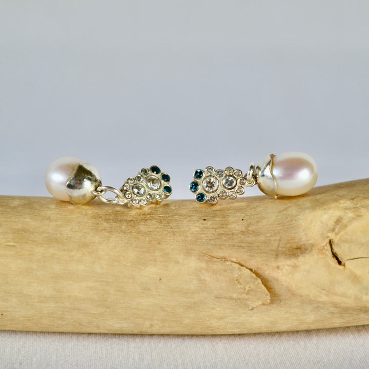 Pair of pearl earrings with gemstones on a wooden surface