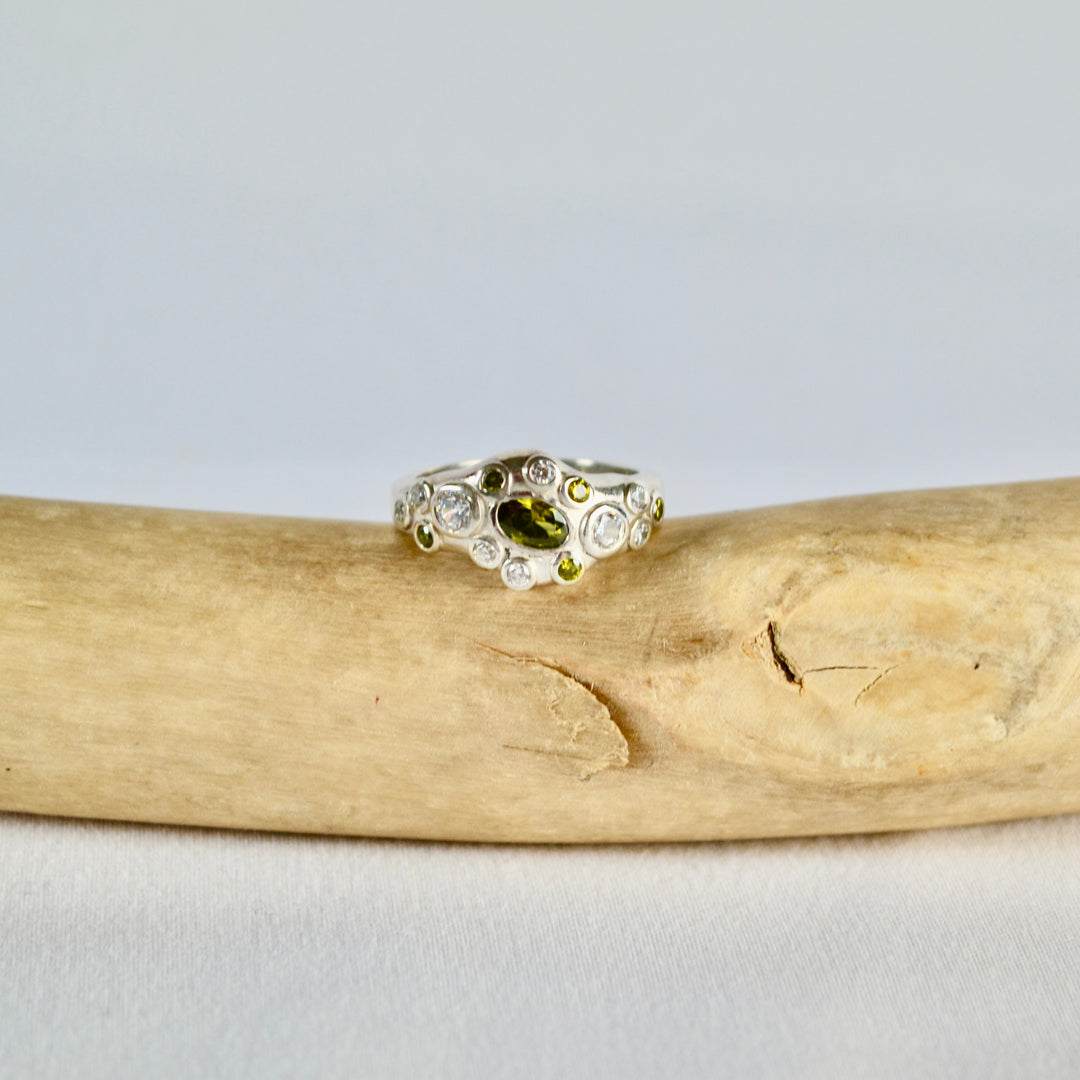 Gold ring with a green gemstone on a piece of driftwood against a light gray background