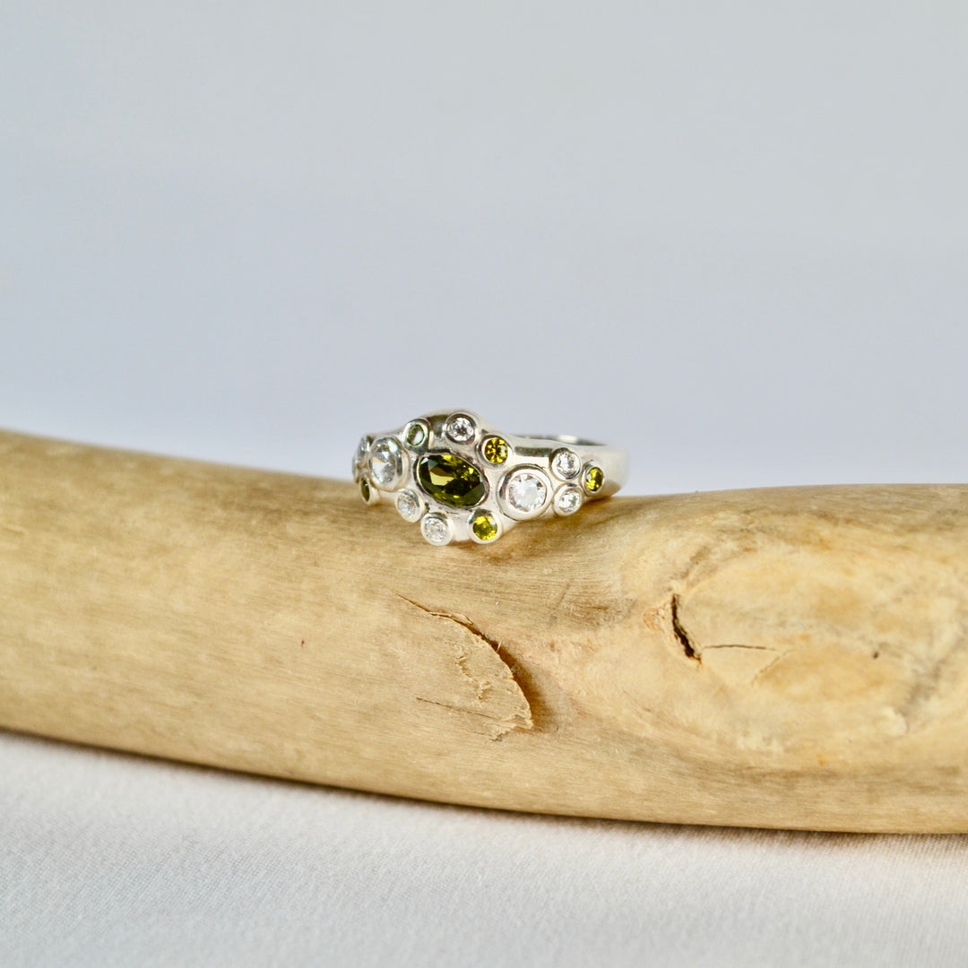 Silver ring with a green gemstone on a piece of driftwood against a light gray background