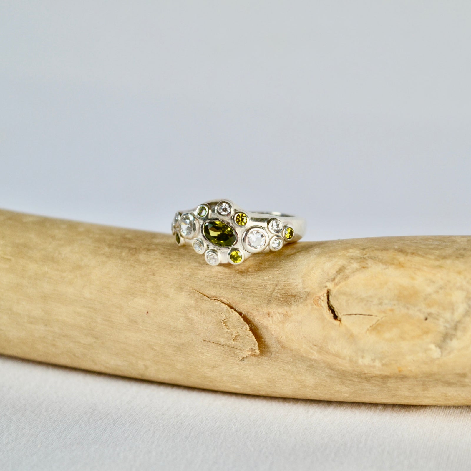 Silver ring with a green gemstone on a piece of driftwood against a light gray background