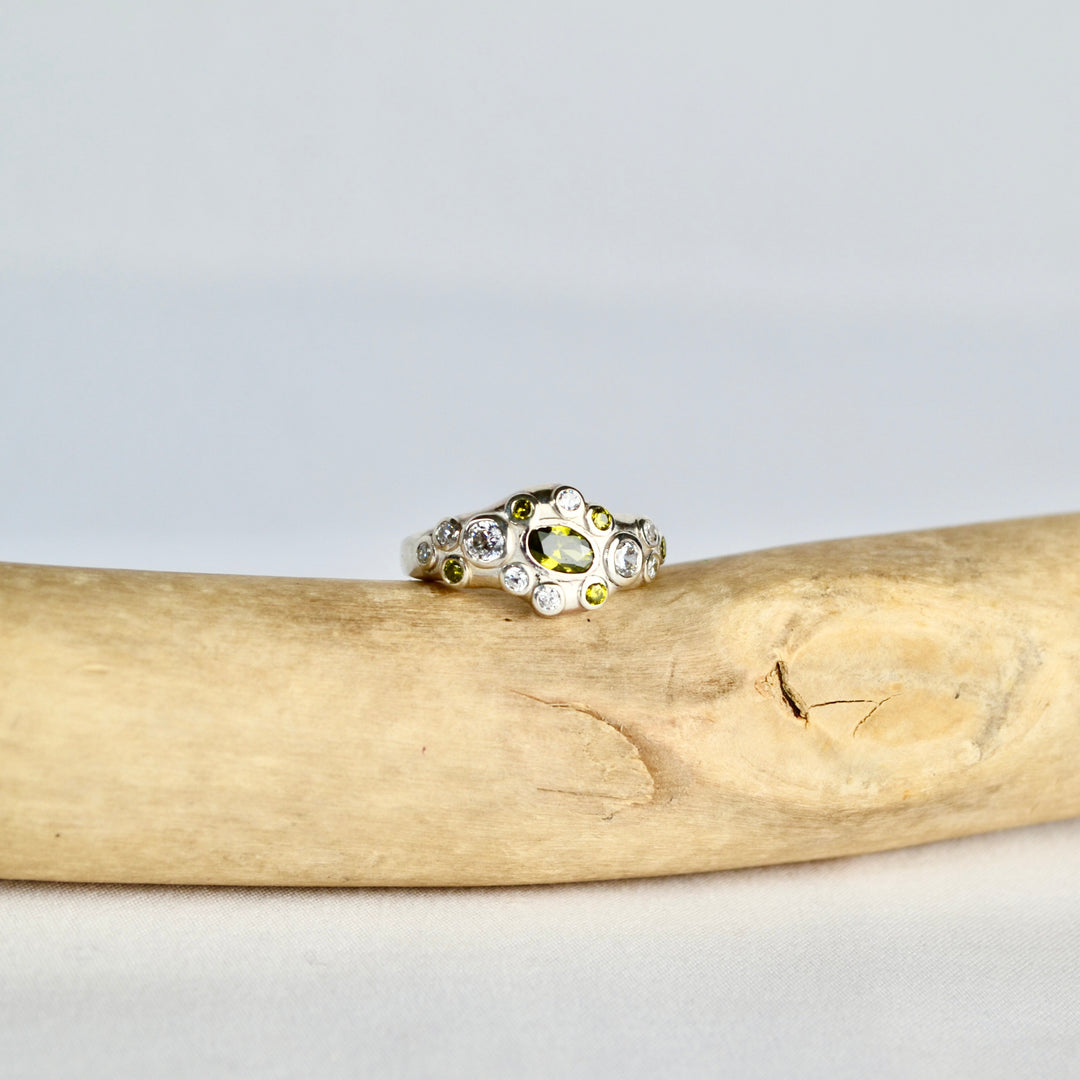 Silver ring with a yellow gemstone on a piece of driftwood against a light gray background