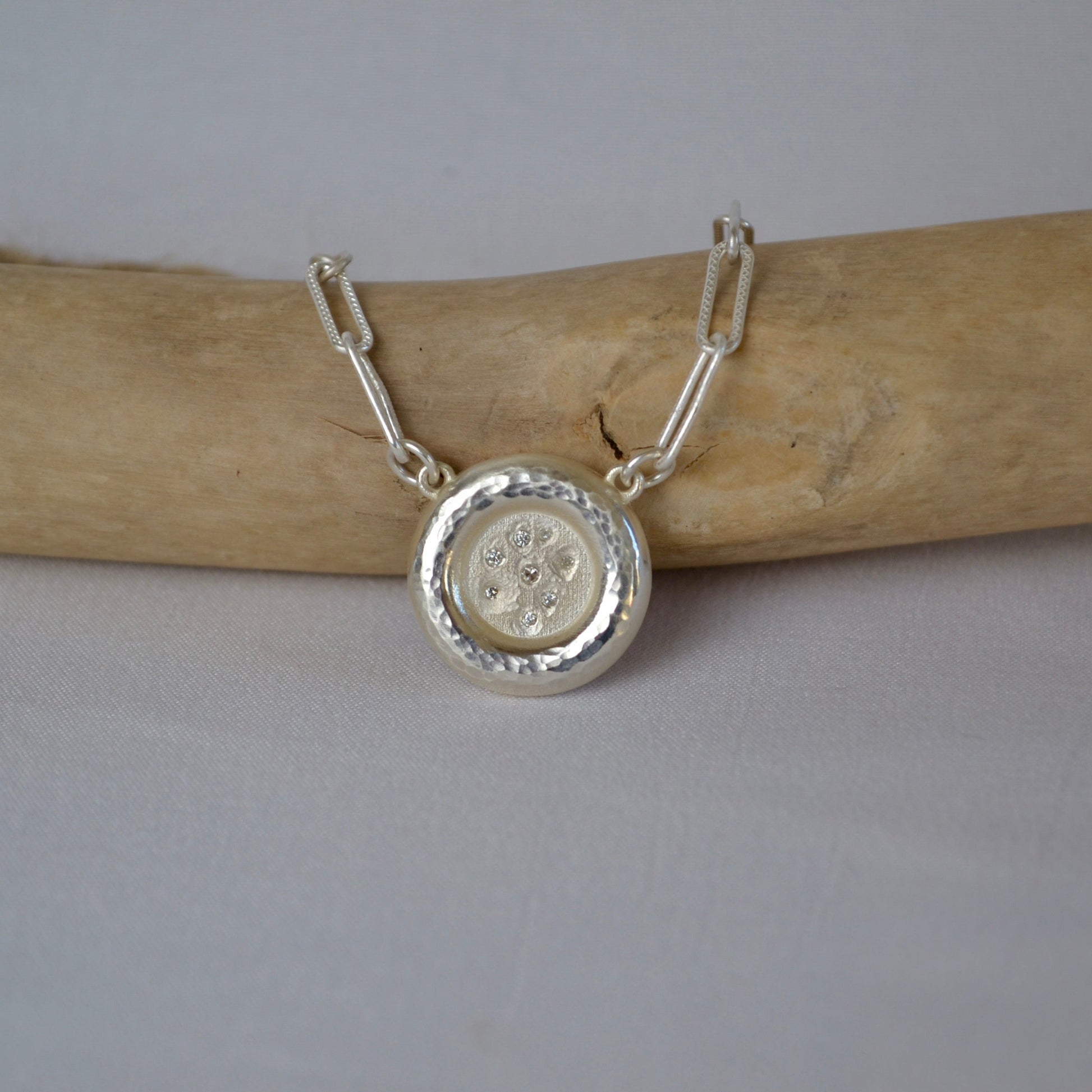 Silver necklace with a round pendant on a wooden stick against a gray background