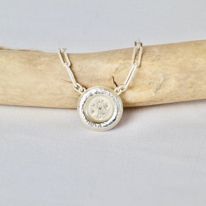 Silver necklace with a round pendant on a light gray background