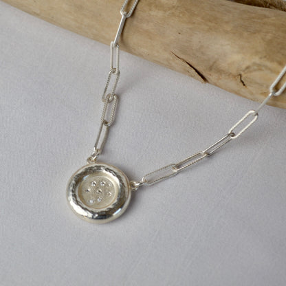 Silver necklace with a round pendant on a light gray background