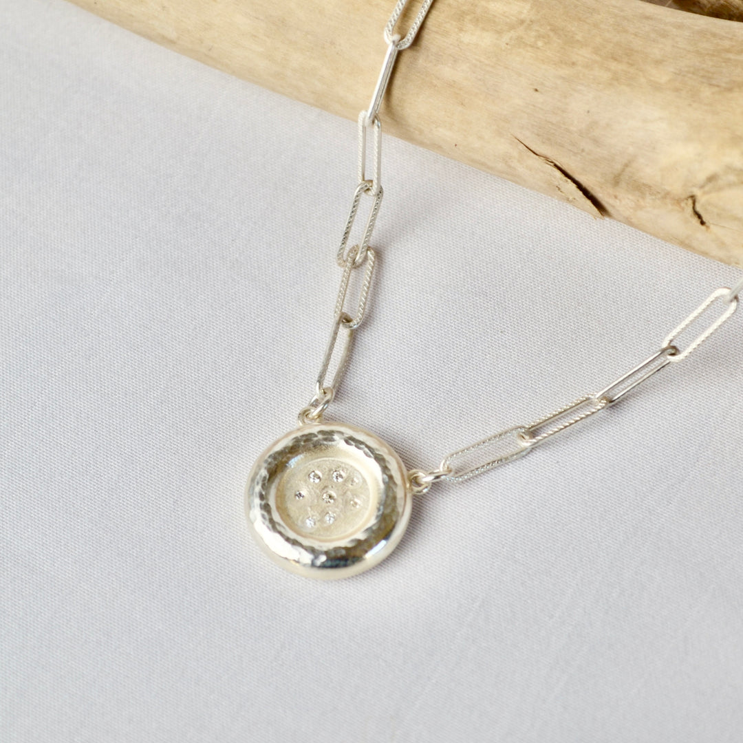 Silver necklace with a round pendant on a light gray background