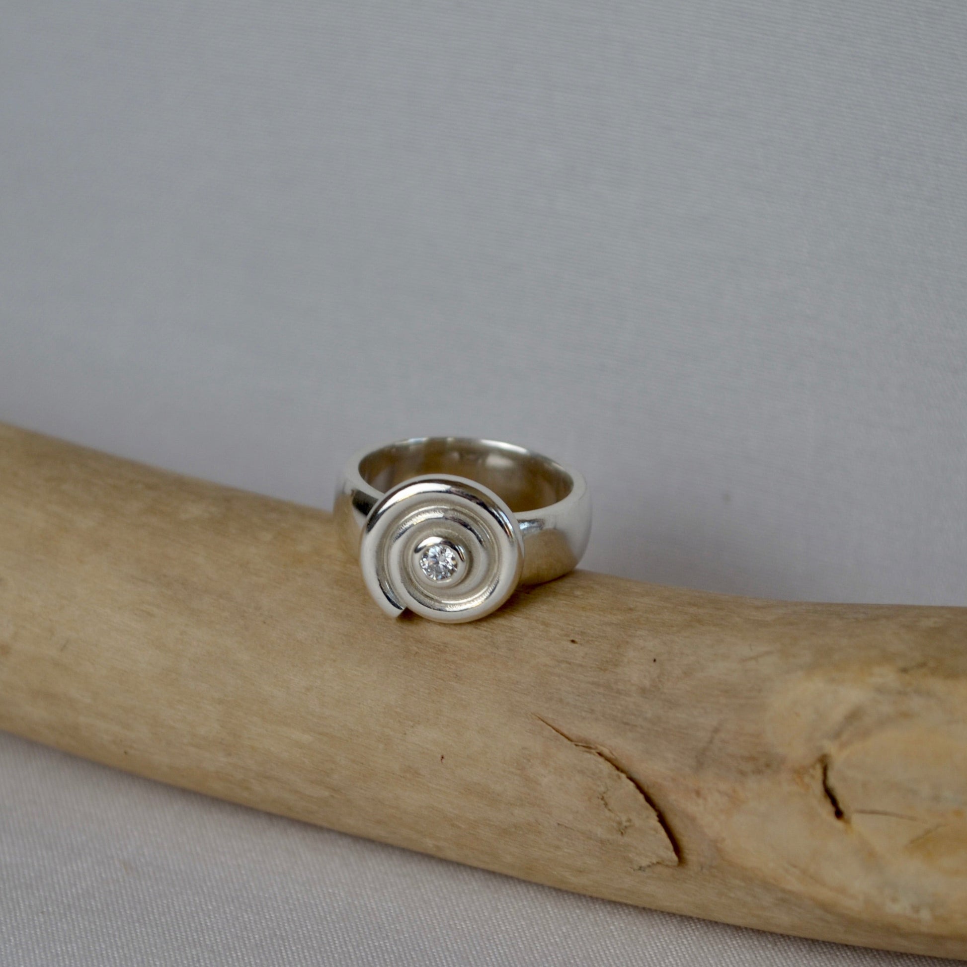 Silver ring with a central gemstone on a piece of driftwood against a gray background