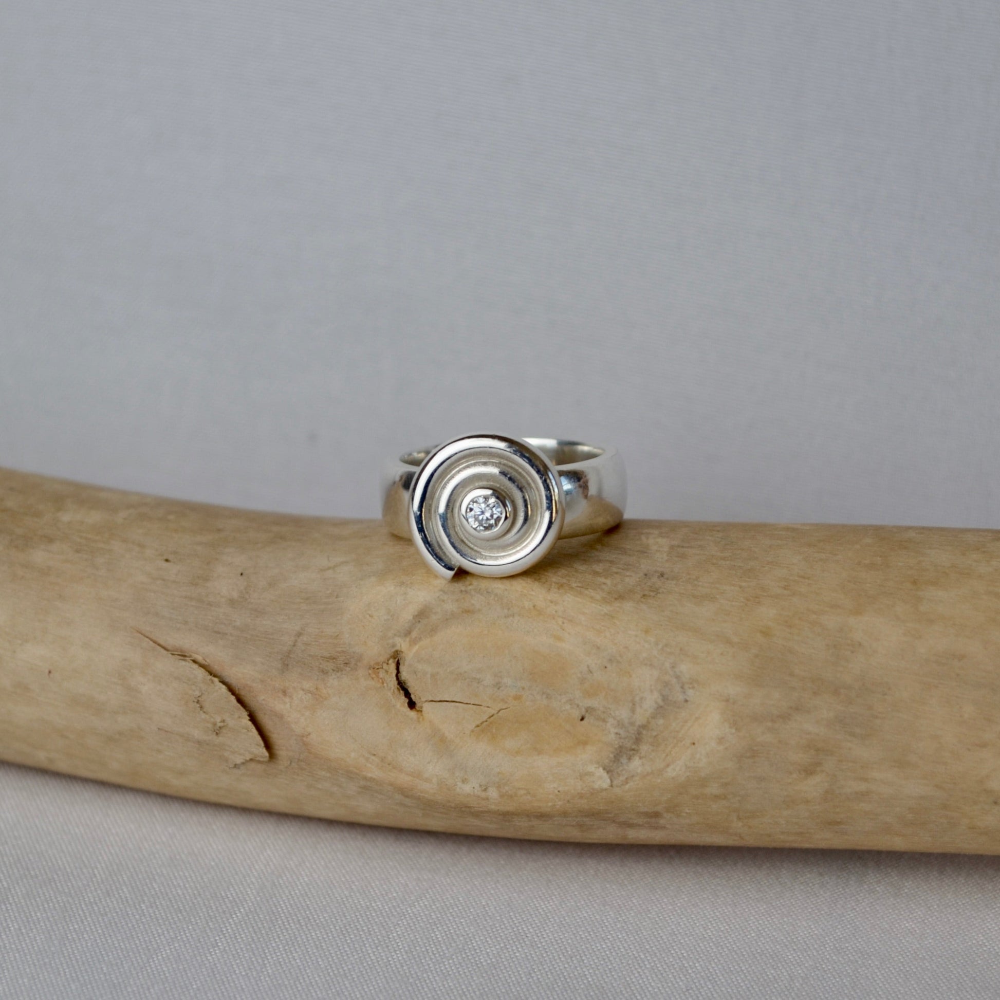 Silver ring with a circular design on a piece of driftwood against a gray background