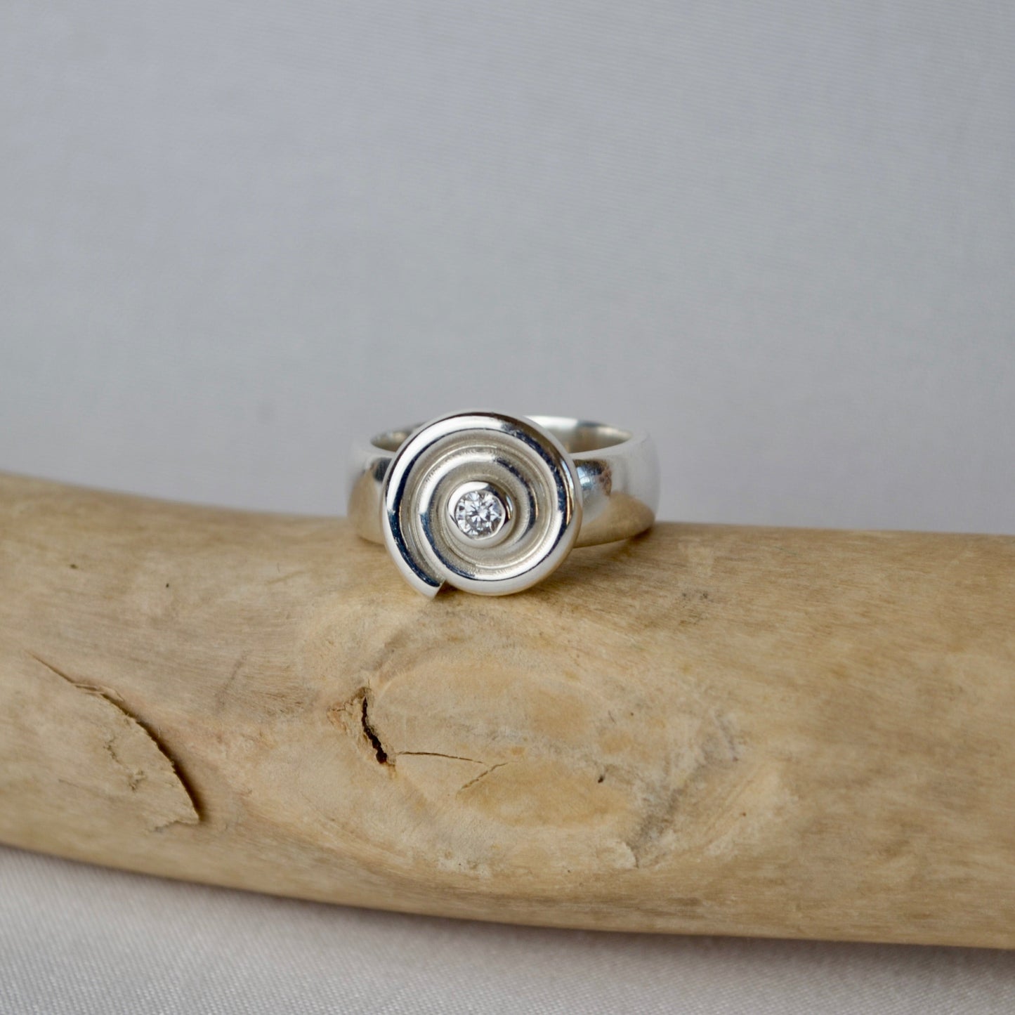 Silver ring with a diamond on a piece of driftwood against a gray background