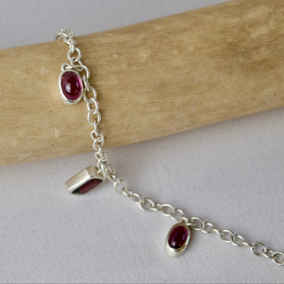 Silver bracelet with red gemstones on a wooden stick