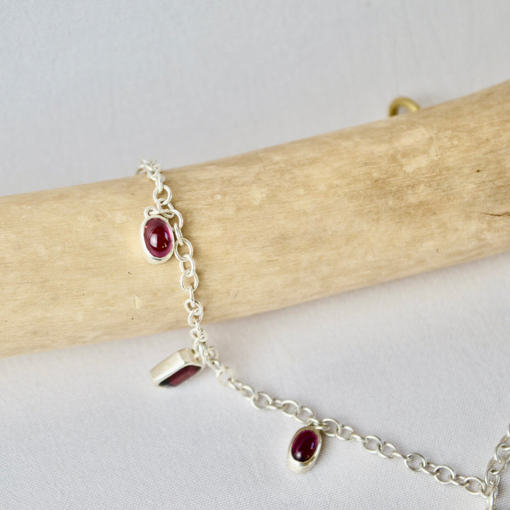 Silver bracelet with red gemstones on a wooden stick