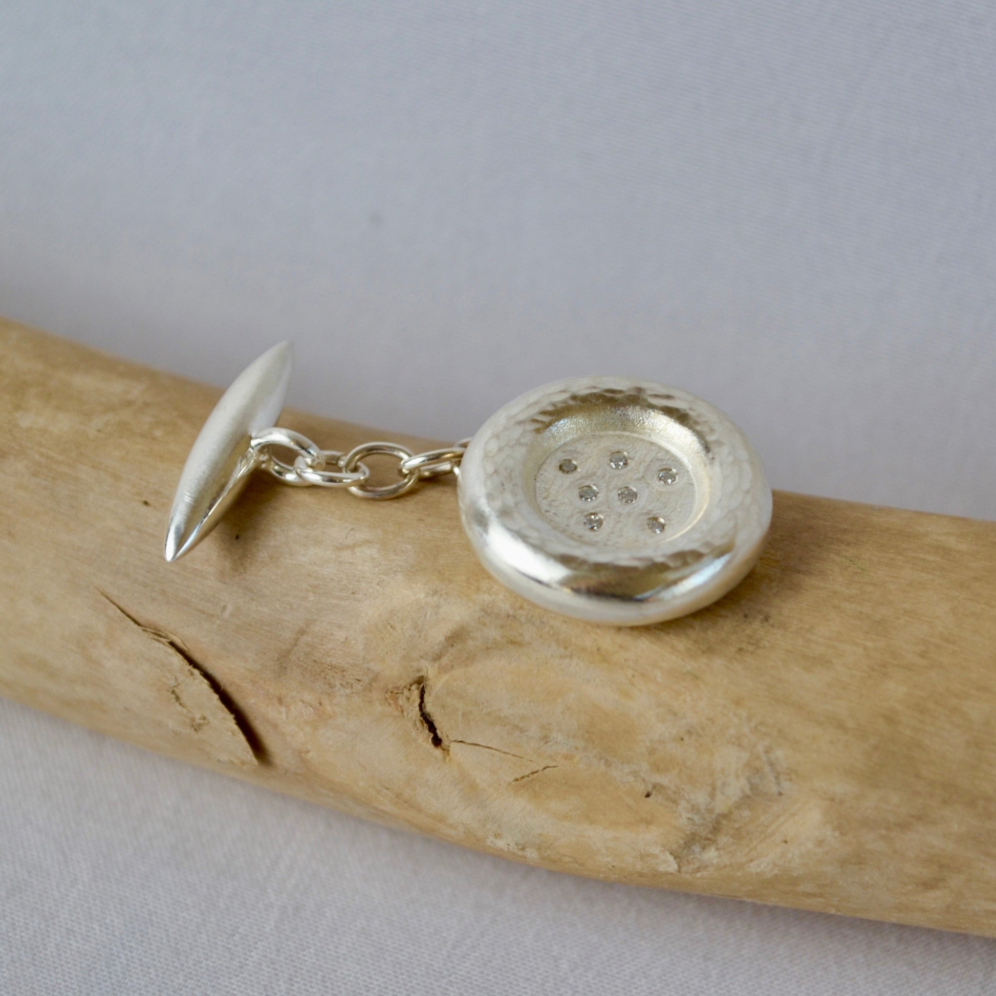 Silver cufflinks on a piece of driftwood with a plain background