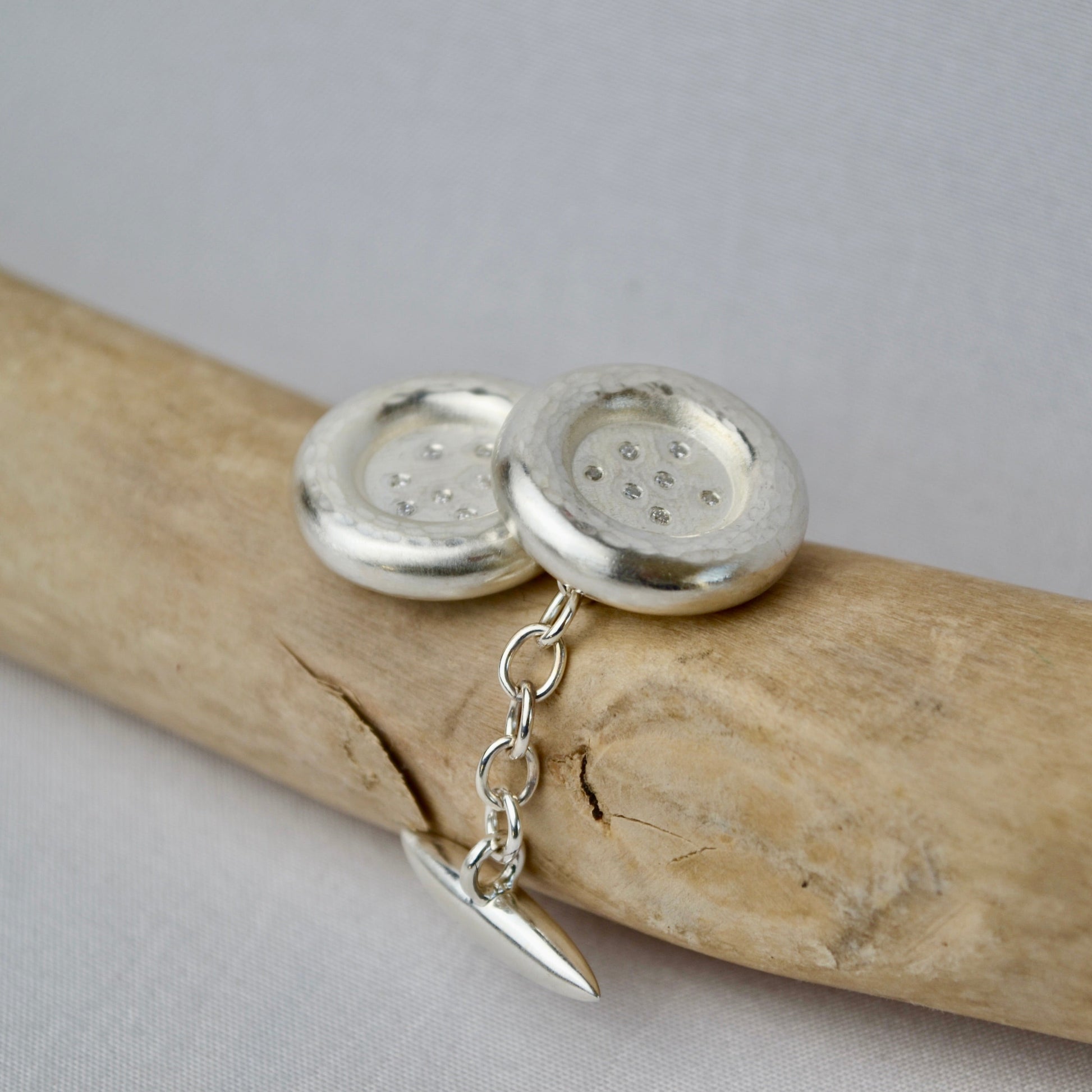 Silver button earrings with a chain on a piece of driftwood.