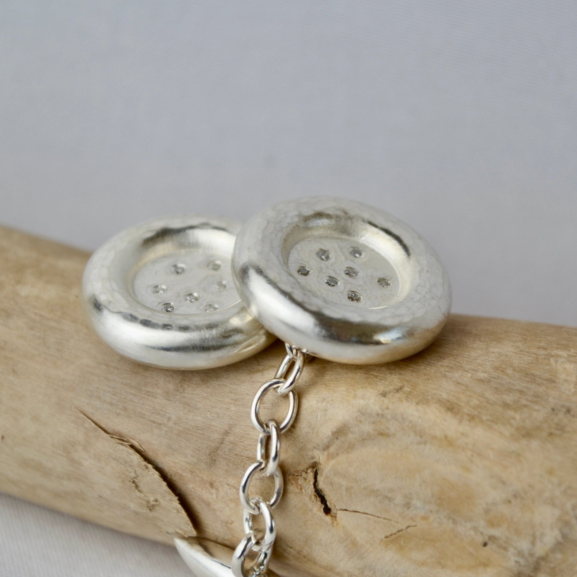 Silver button cufflinks on a piece of wood with a neutral background