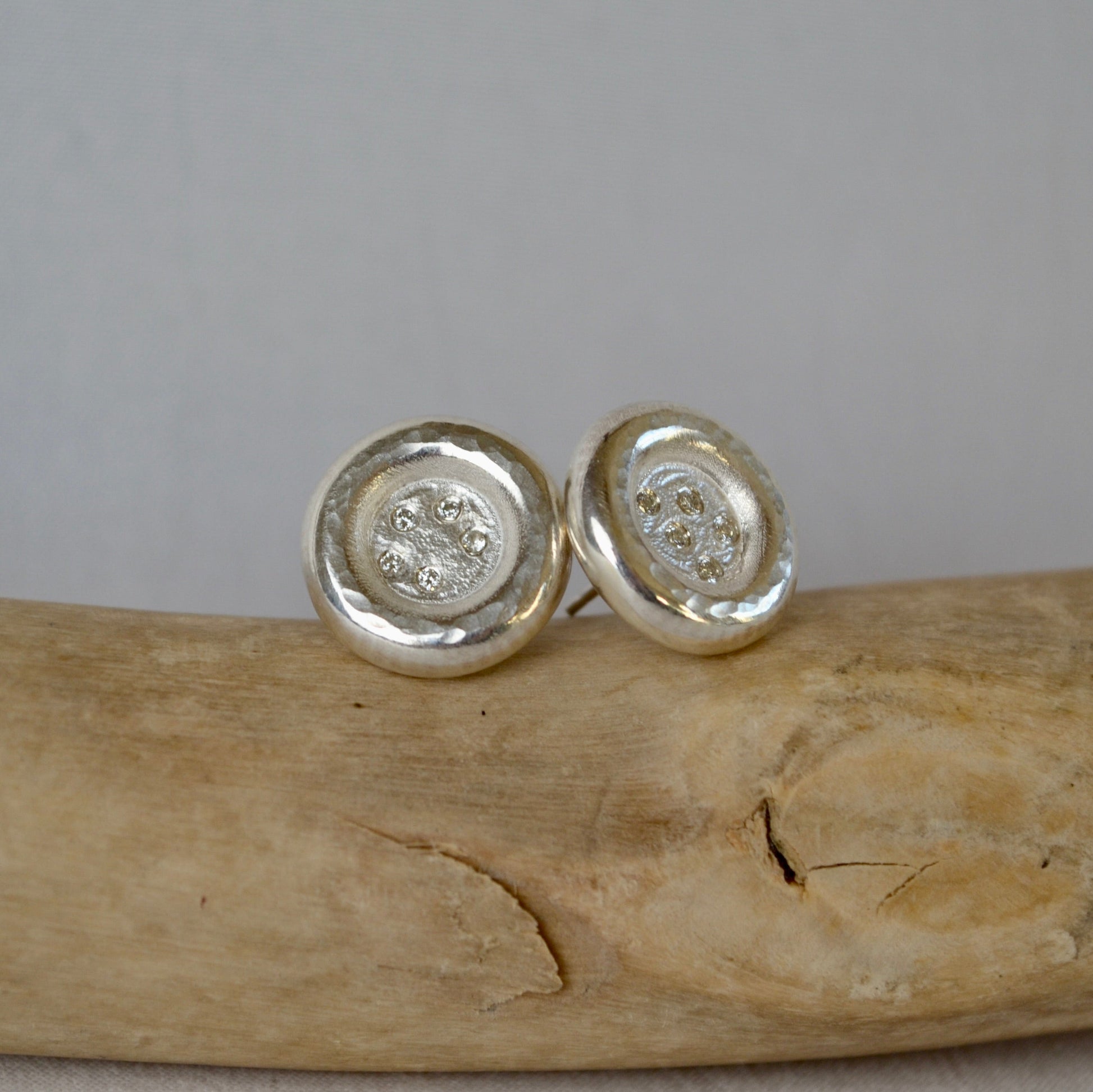 Silver round earrings on a wooden surface with a gray background