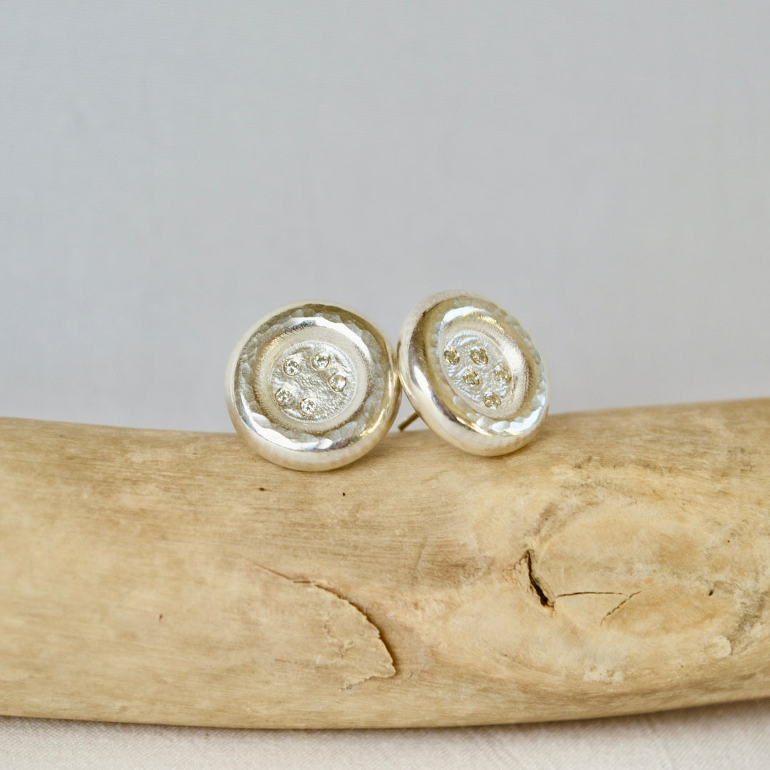 Silver circular earrings on a piece of driftwood with a neutral background