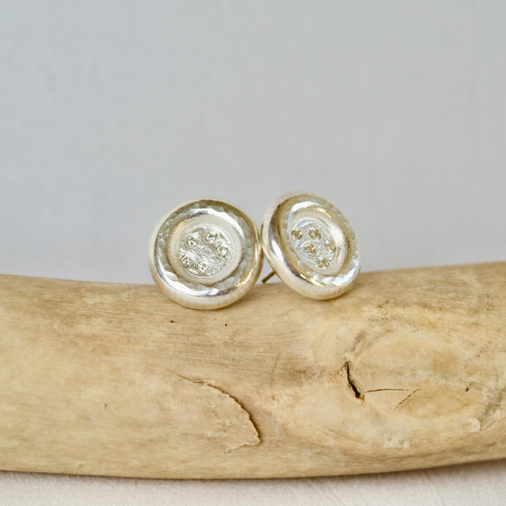 Silver circular earrings on a piece of driftwood with a neutral background