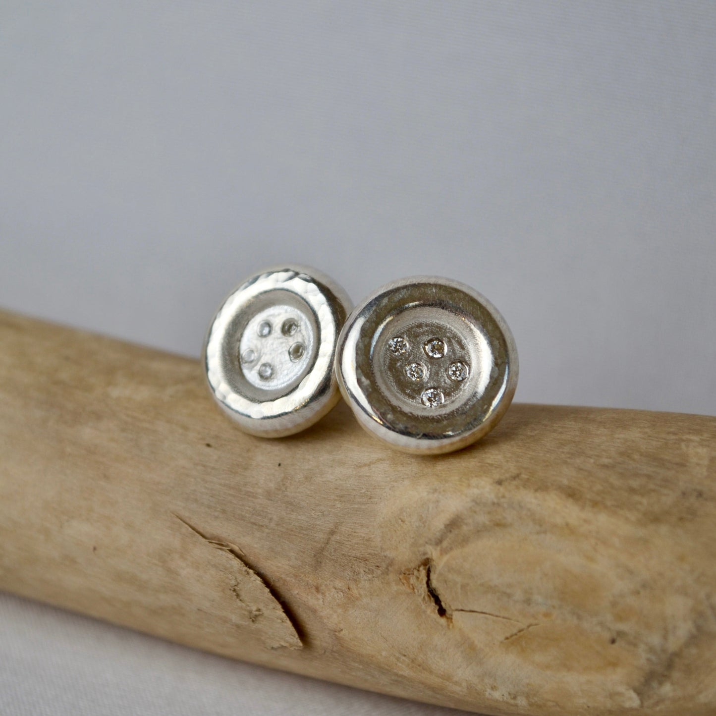 Silver button earrings on a wooden surface with a gray background