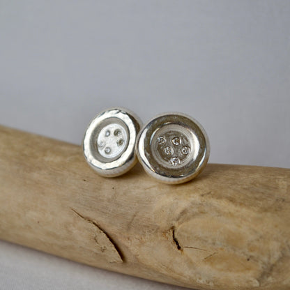 Silver button earrings on a wooden surface with a gray background