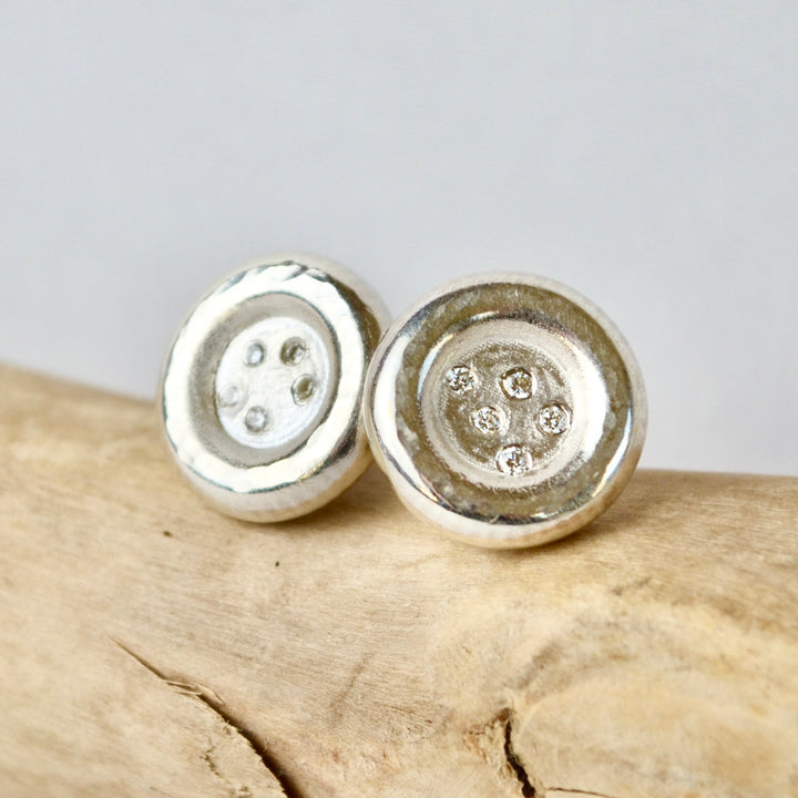 Silver button earrings on a wooden surface with a light gray background