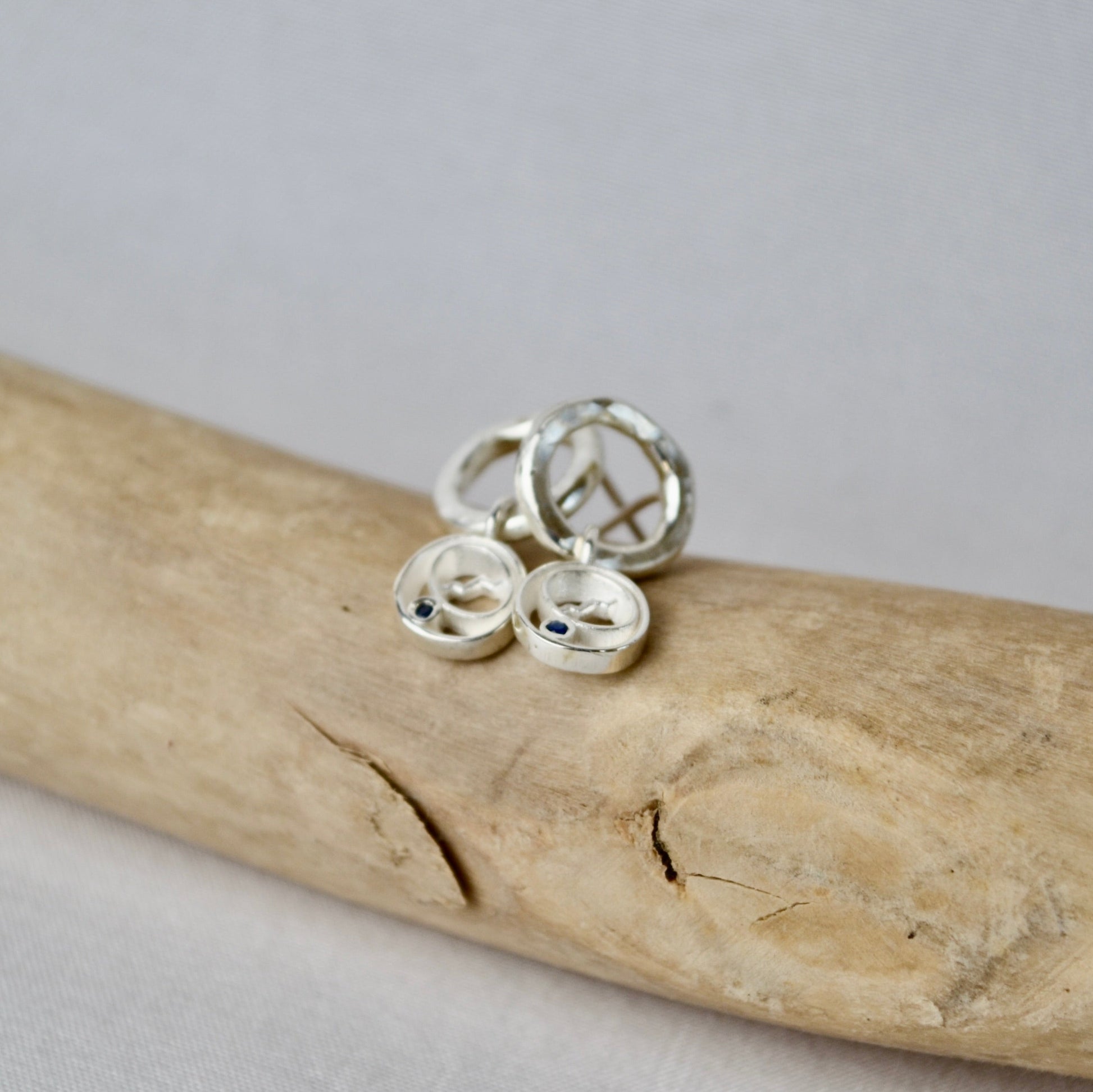 Three silver rings on a piece of driftwood with a plain background