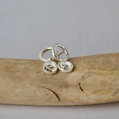 Silver earrings on a piece of driftwood with a neutral background