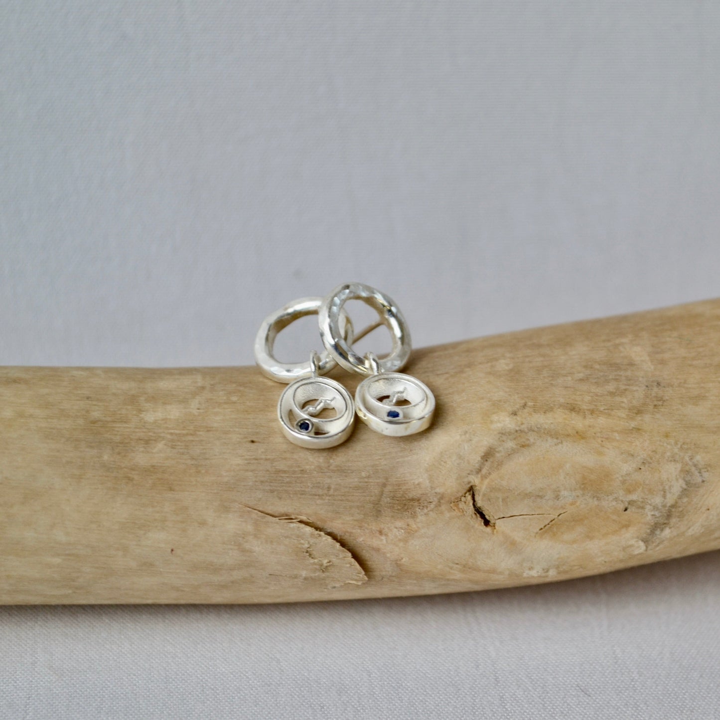Silver button earrings on a piece of driftwood with a gray background